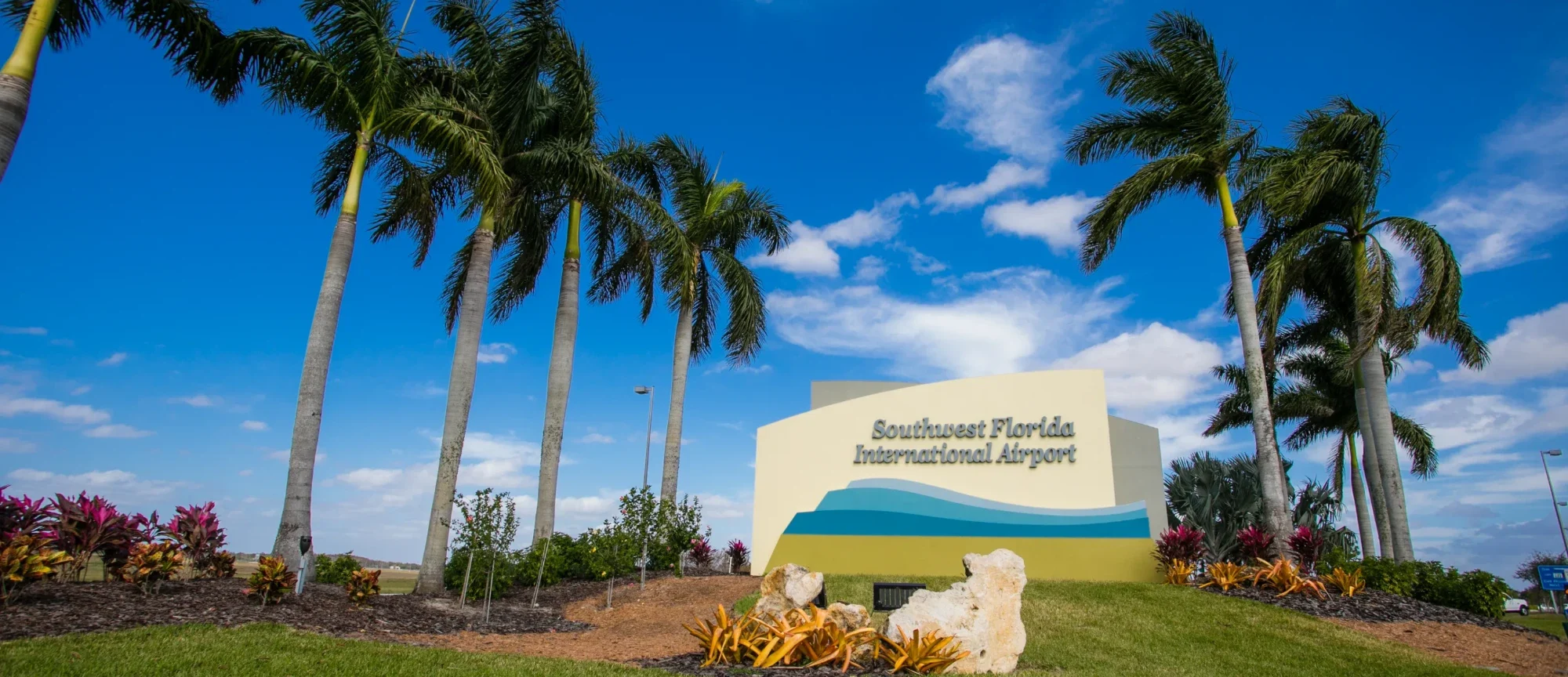 The Southwest Florida International Airport entrance sign framed by royal palms under a blue sky